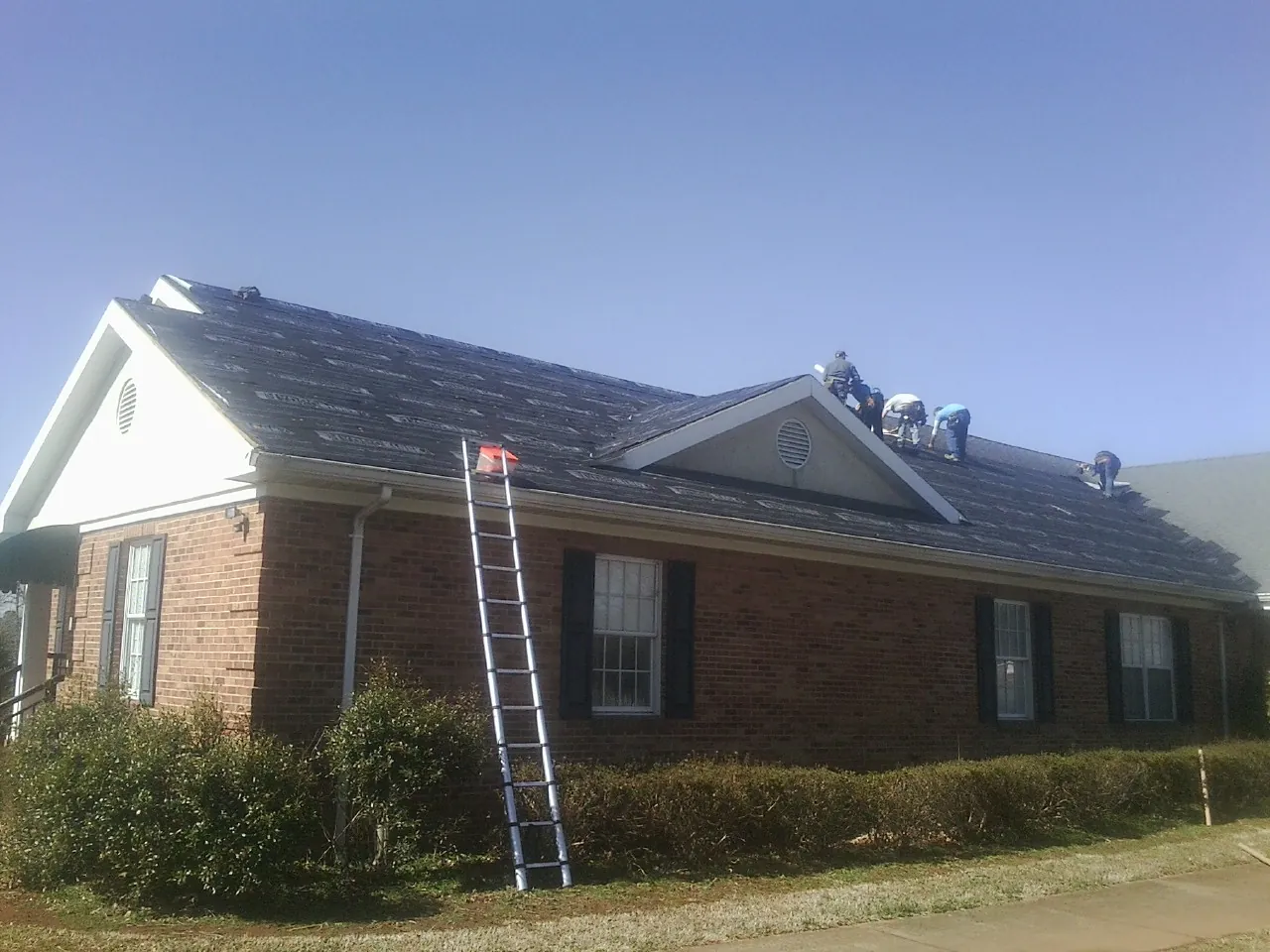 Crew tearing shingles off a brick ranch roof with a ladder set — Metal Roof Repair work by our crew in Delta