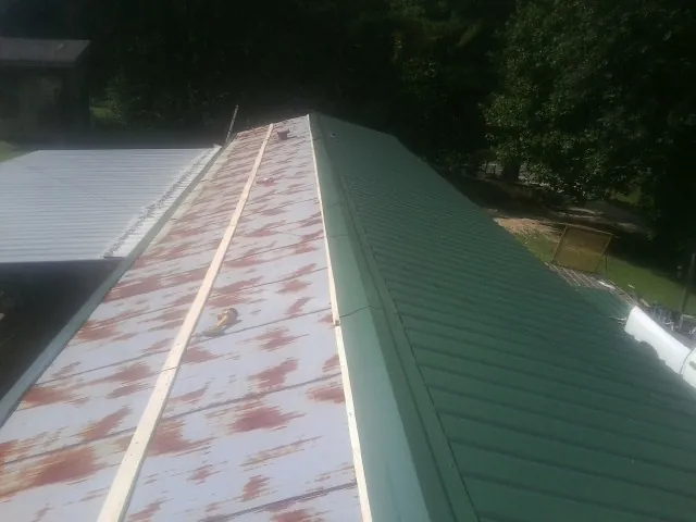 Old rusted panels beside newly installed green metal roofing — Wind Damage Roof Repair by Roofing Brothers in Delta